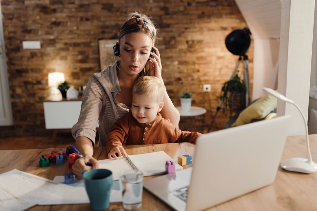 Une mère de famille gérant son ordinateur de travail à la maison tout en s'occupant de son jeune enfant.